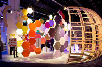 Custom booth design with colorful hexagonal panels and a unique wooden arch structure at a trade fair