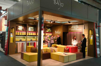 Warm, inviting booth with home decor and textiles displayed in a comfortable lounge setting at Heimtextil trade fair